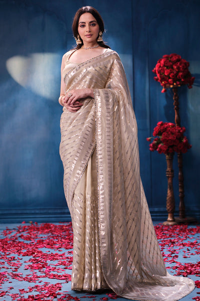 Woman in a beige saree standing on a blue background with red flowers and petals.