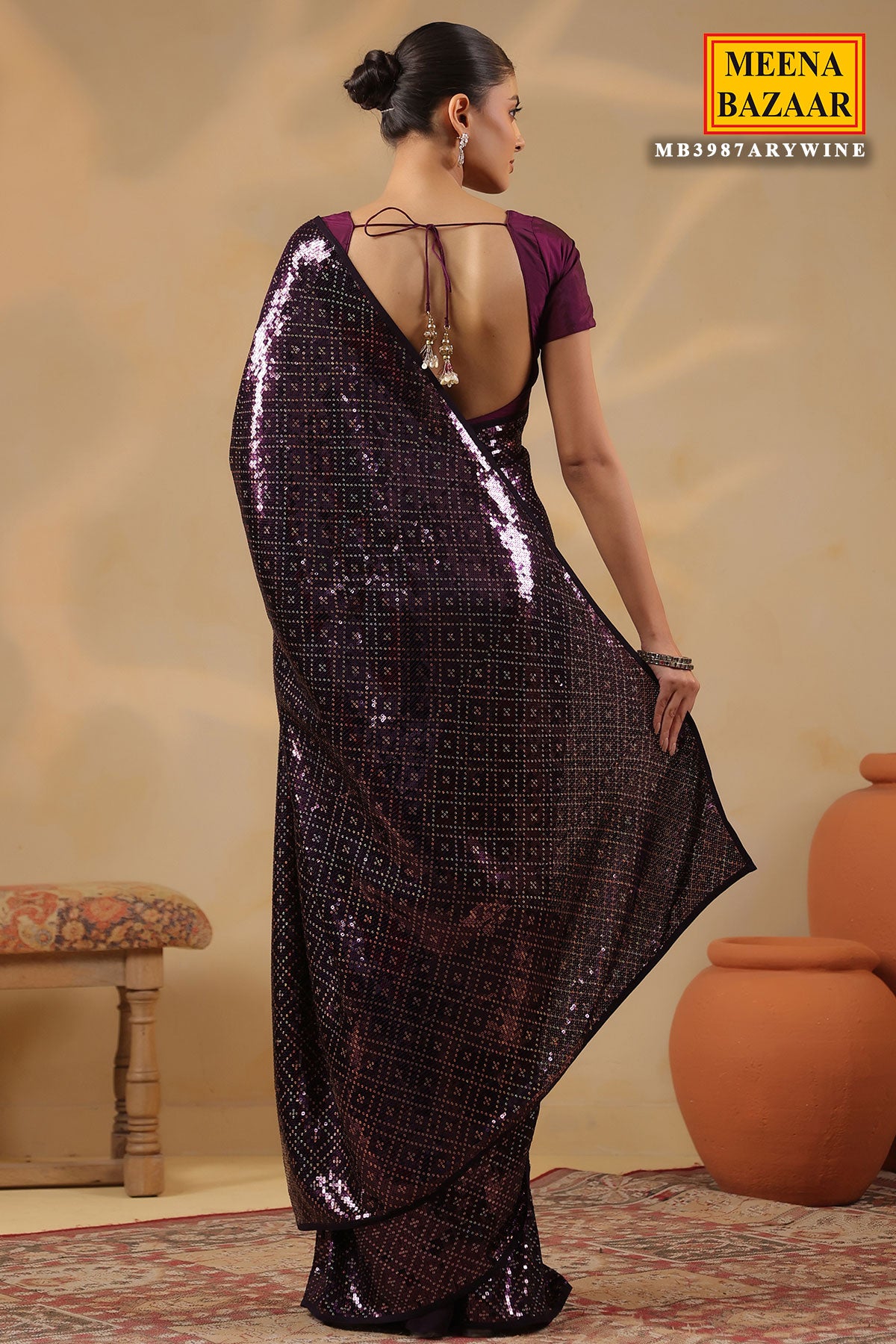Woman wearing a dark purple saree with a pattern, standing against a neutral background with 'Meena Bazaar' branding.